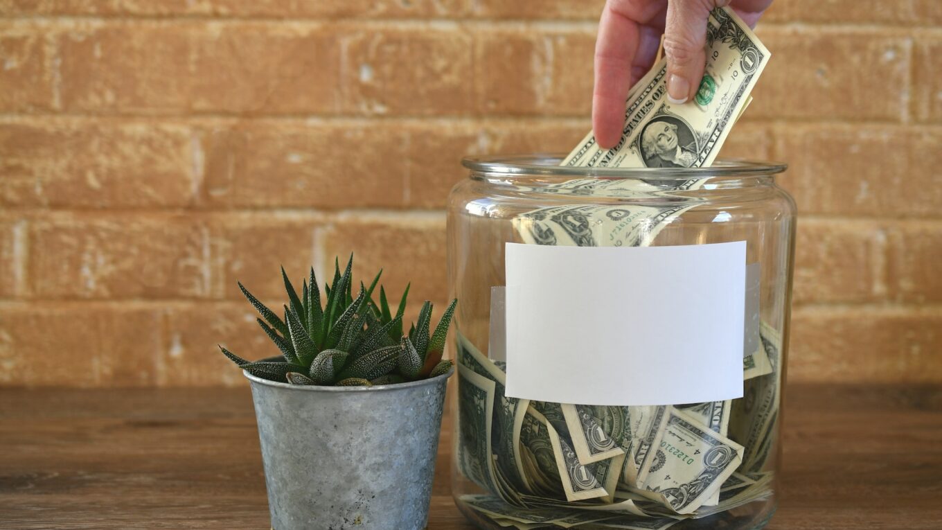 Jar of money cash for donations, contributions, tips, collection - hand in frame - blank copy space